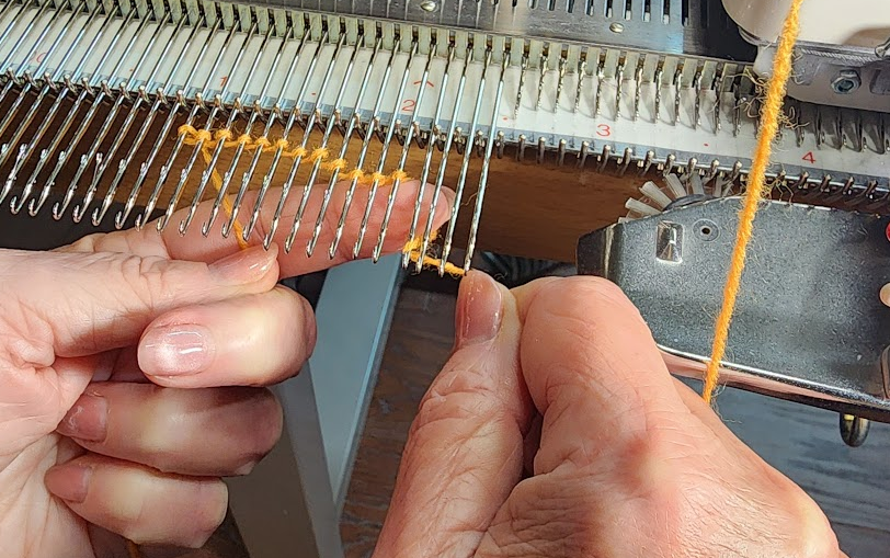 Close-up of hands casting on stitches on a knitting machine